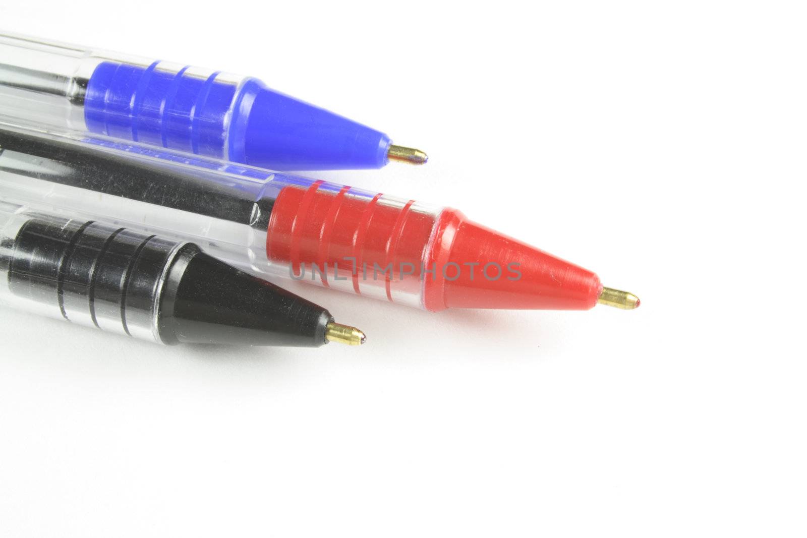 closeup of three different coloured ball point pens isolated over white