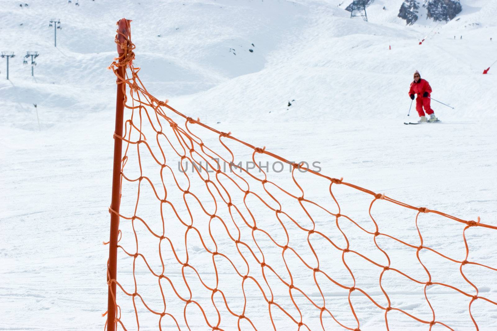 Red fence at ski slope with moving skier at background