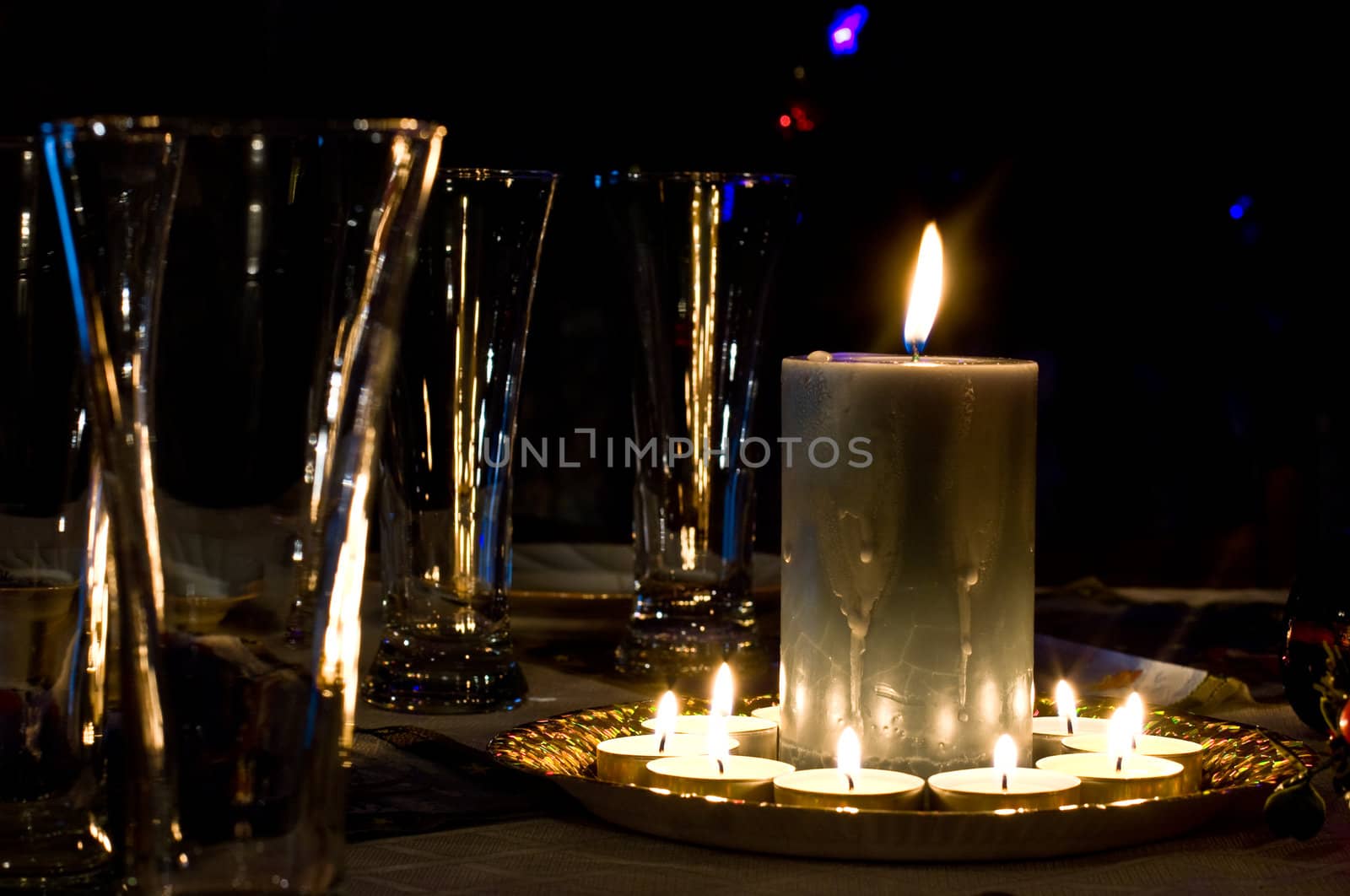 Glasses and burning candles on a table against a black background