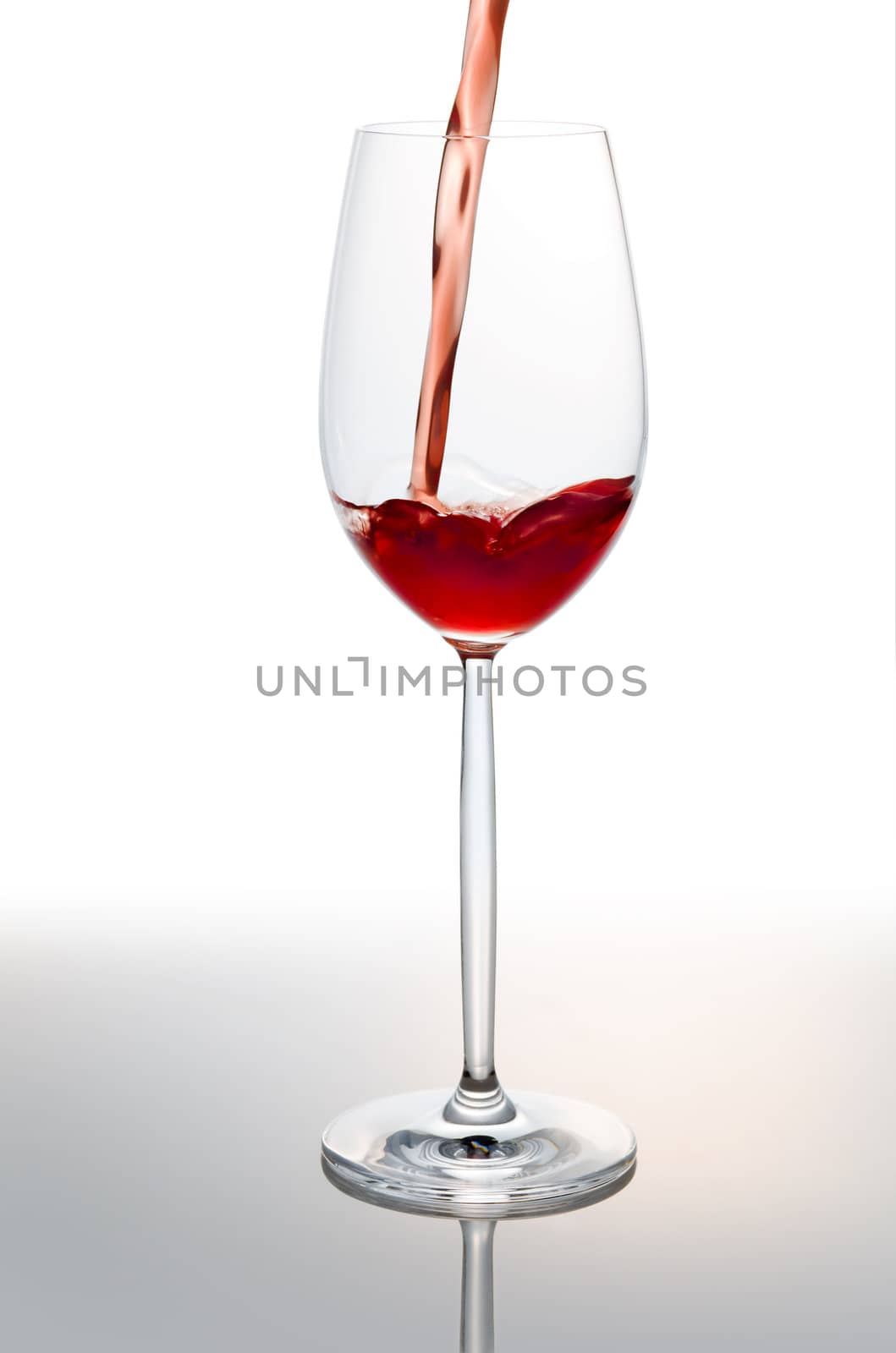 Pouring red wine into glass over a mirror 