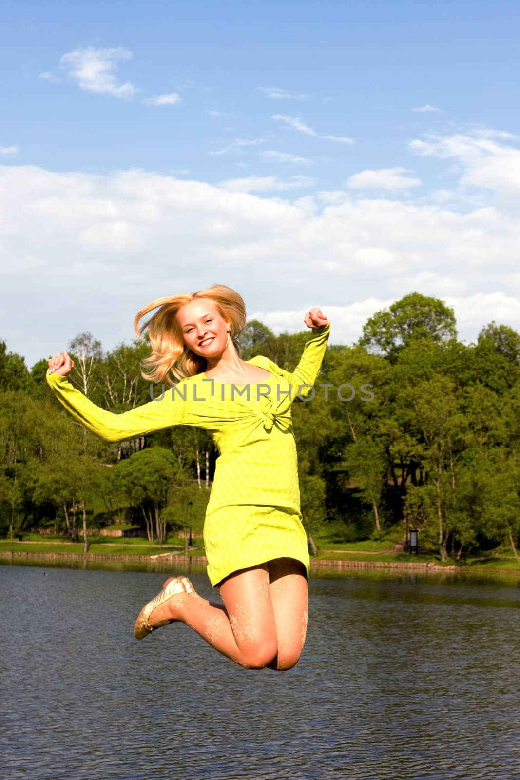 The happy girl jumps on the bank of the summer river