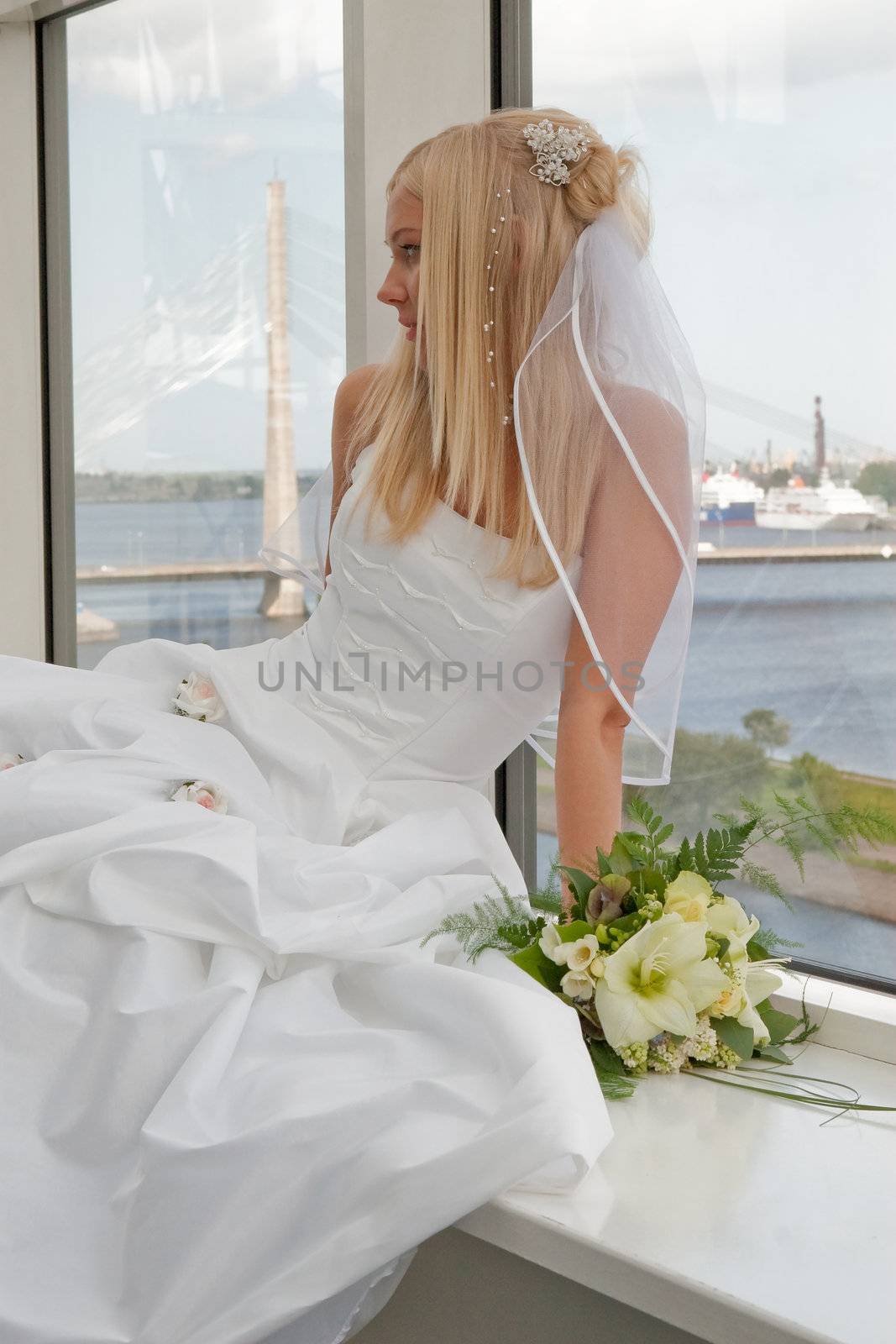 Beautiful blonde bride with bunch of flowers on the window