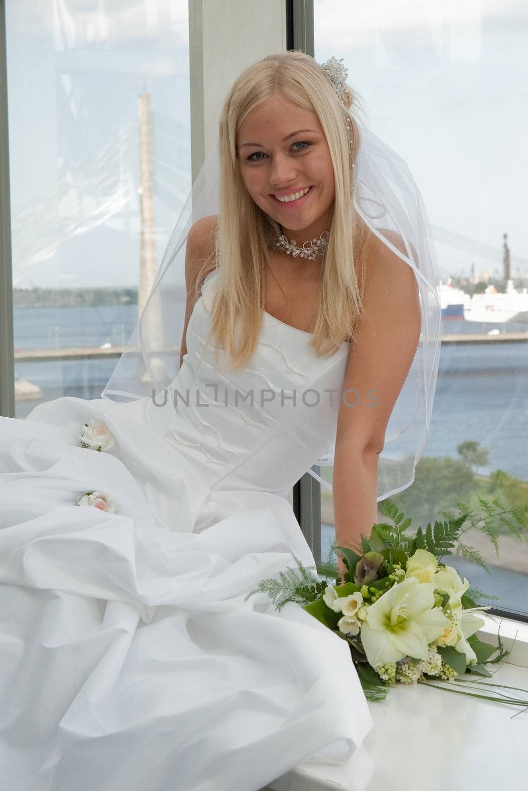 Beautiful blonde bride with bunch of flowers on the window