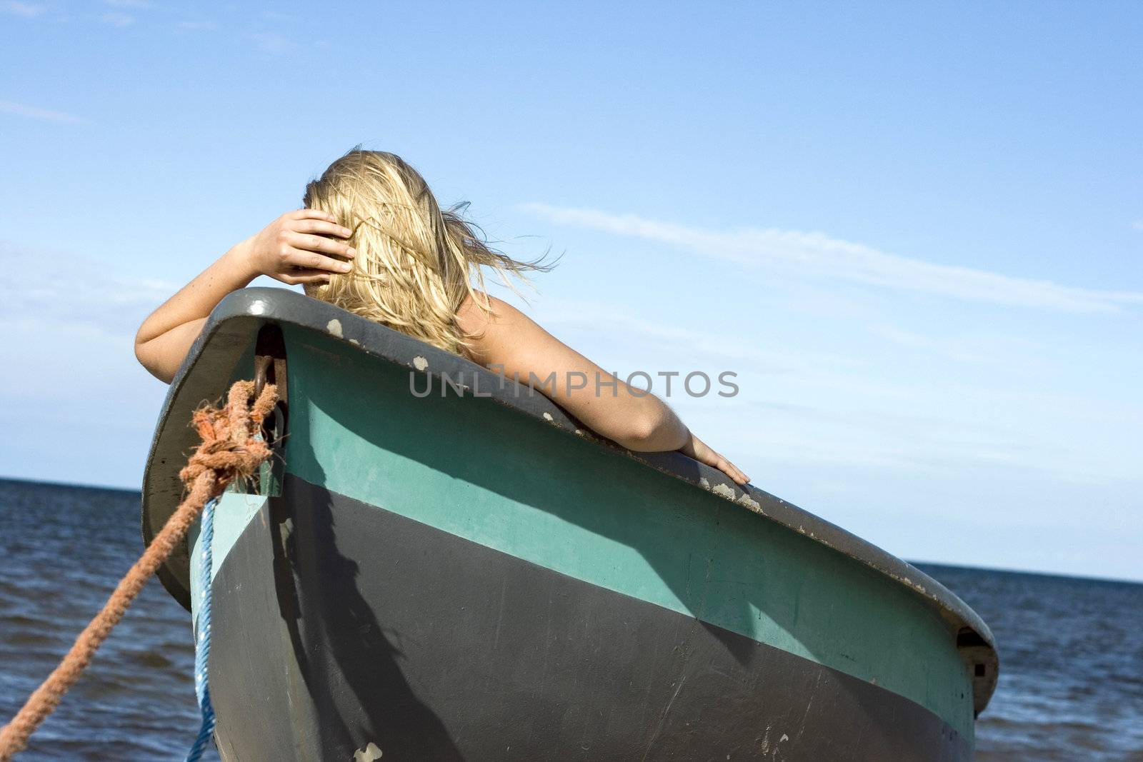 Young woman sitting in old fisherman's boat and looking to the sea.