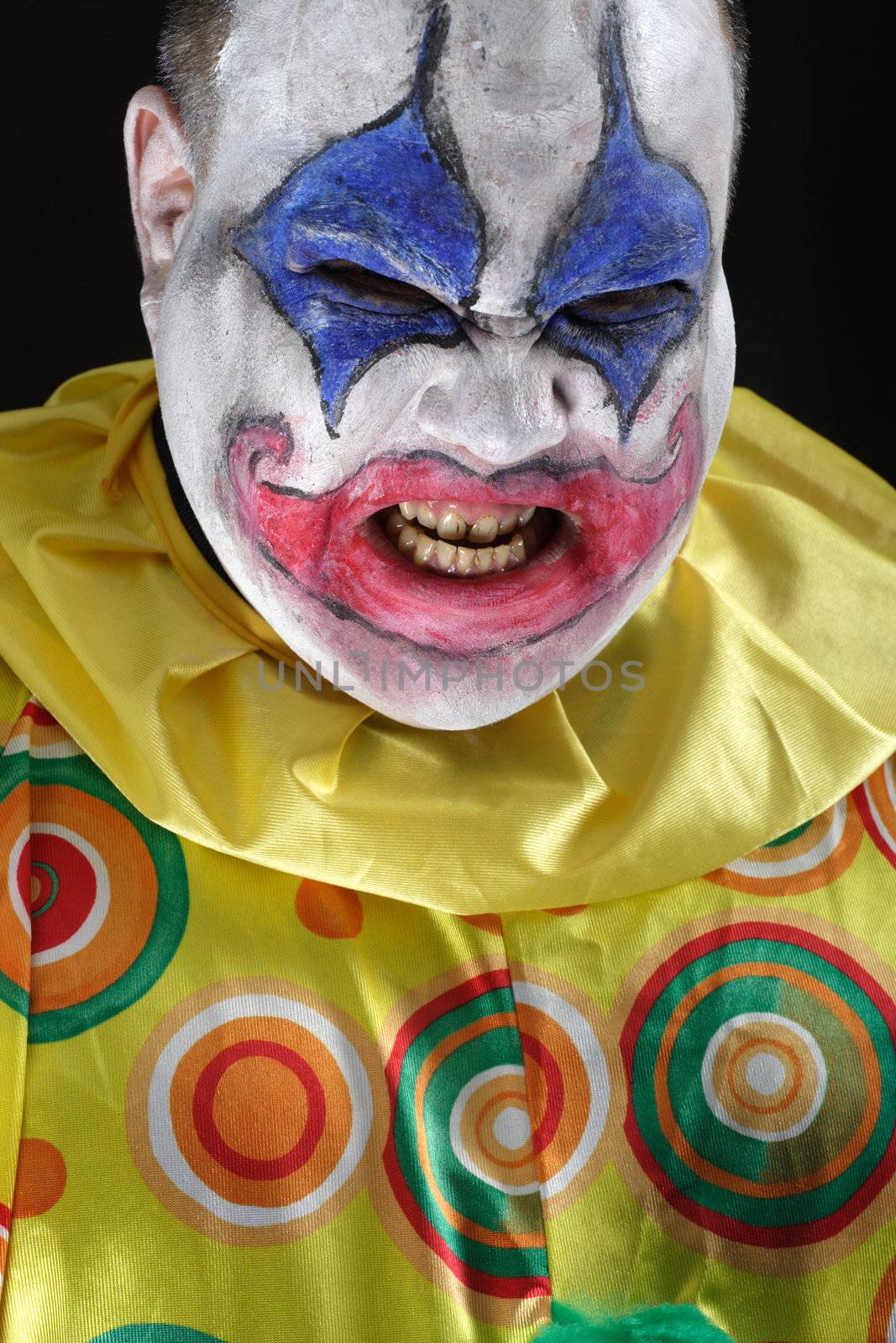 A nasty evil clown, angry and looking mean. Harsh lighting from below, focus on the teeth.

