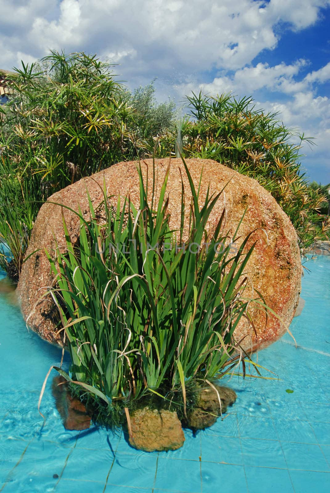 Fountain with a big boulder, decorative reed and a blue sky 