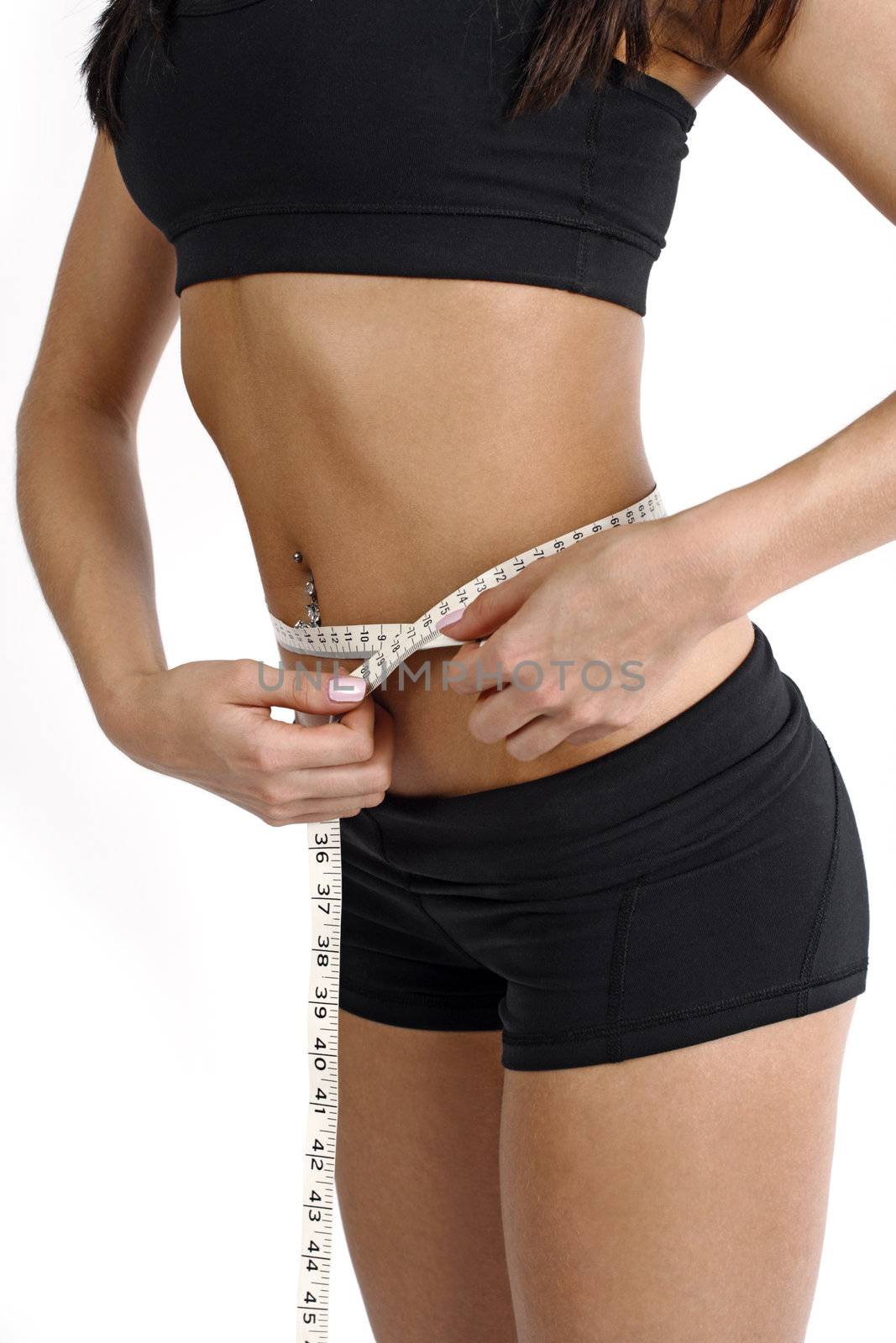 A tanned slim young woman measuring her waistline.
