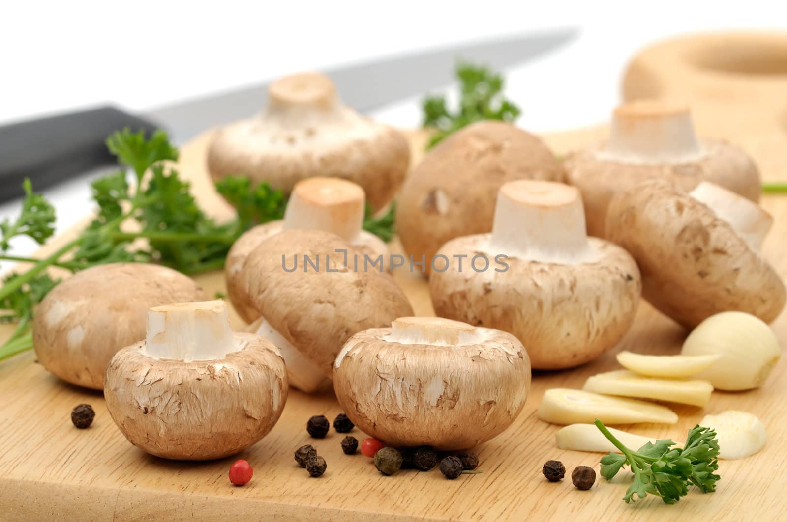 Raw ingredients on a wooden cutting board: mushrooms, parsley, whole pepper and garlic
