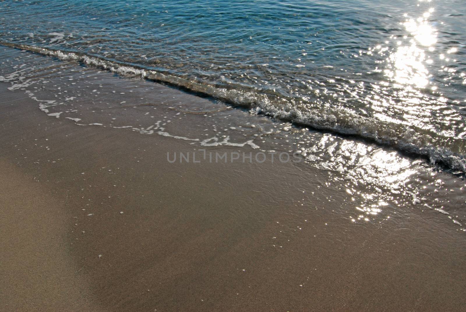 Azure blue tropical sea with waves and an empty beach with a sun reflecting in water