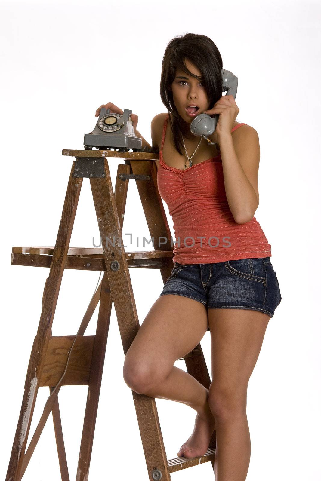 teenage girl standing barefoot on ladder talking on a old rotary phone with a surprise expression