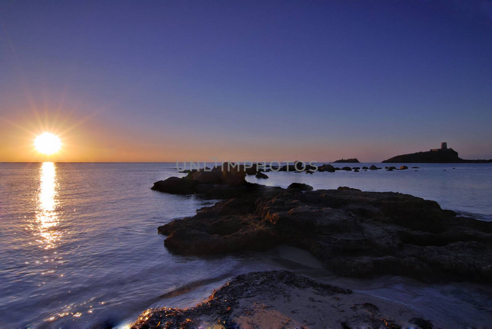 Sunrise in Sardinia with distant lighthouse and stone pier