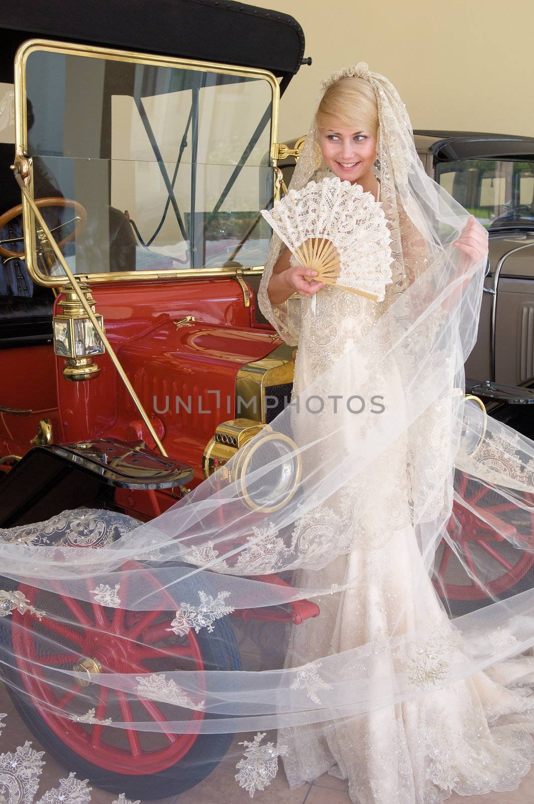 Beautiful bride with fan standing next antique car.