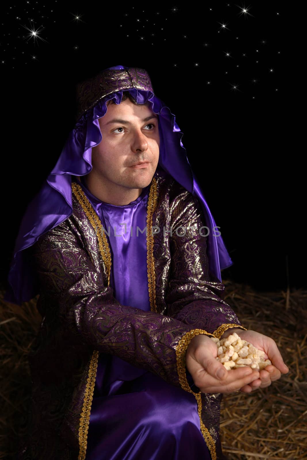 Wise man arrayed in majestic purple robe woven with gold metallic thread is offering in his palms finest pure frankincense. Focus to face.