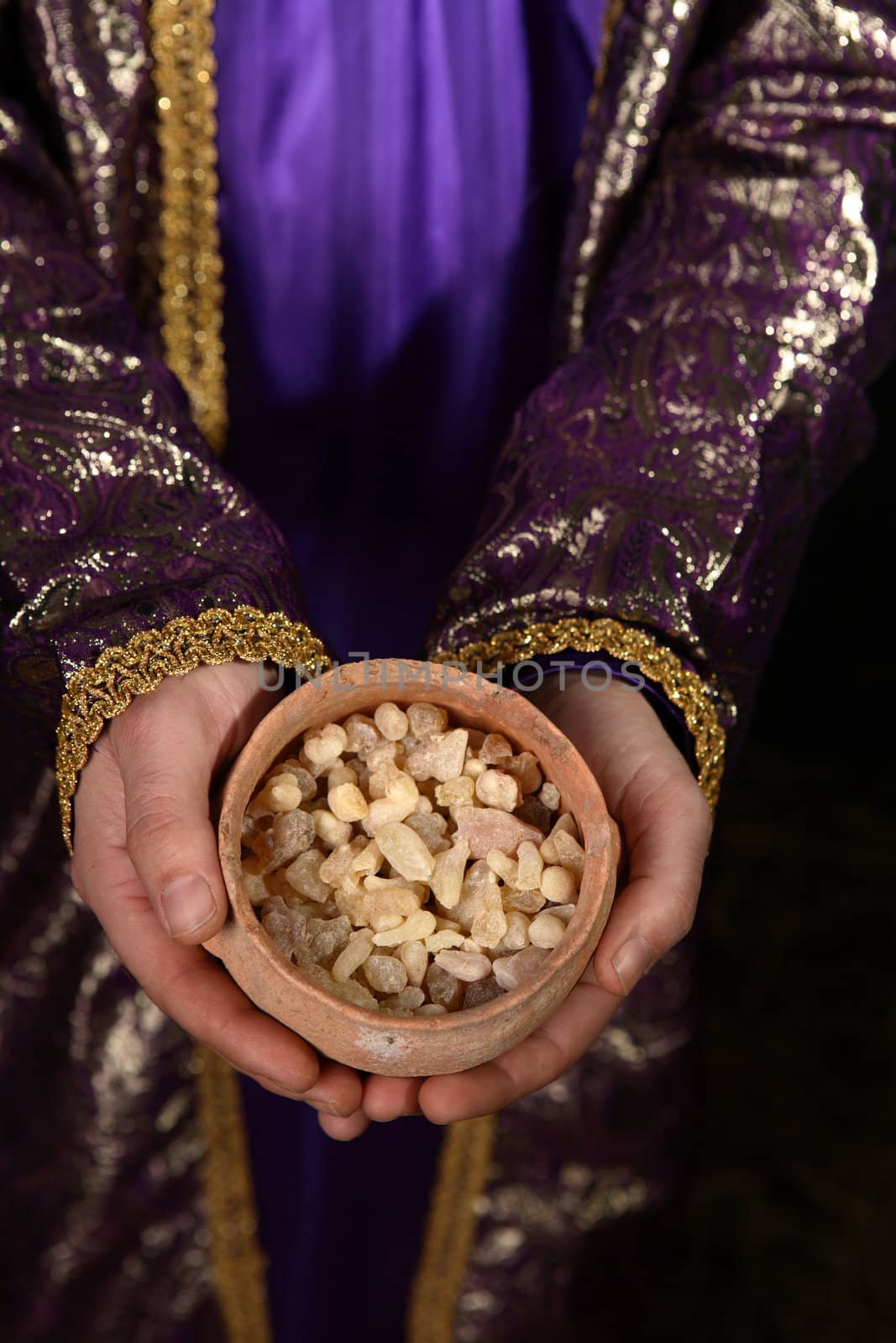 Wise man arrayed in purple cloak embrodered with metallic gold thread, his hands holding an ancient clay pot filled with the best hojari frankincense resin tears from dhofar region of Oman.  The aroma is warm and citrusy