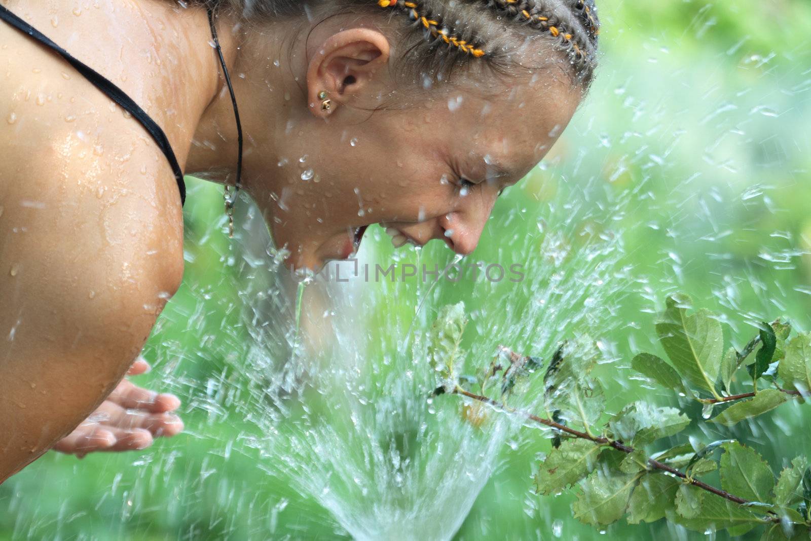 Beautiful girl washing her face with splashing water on nature background