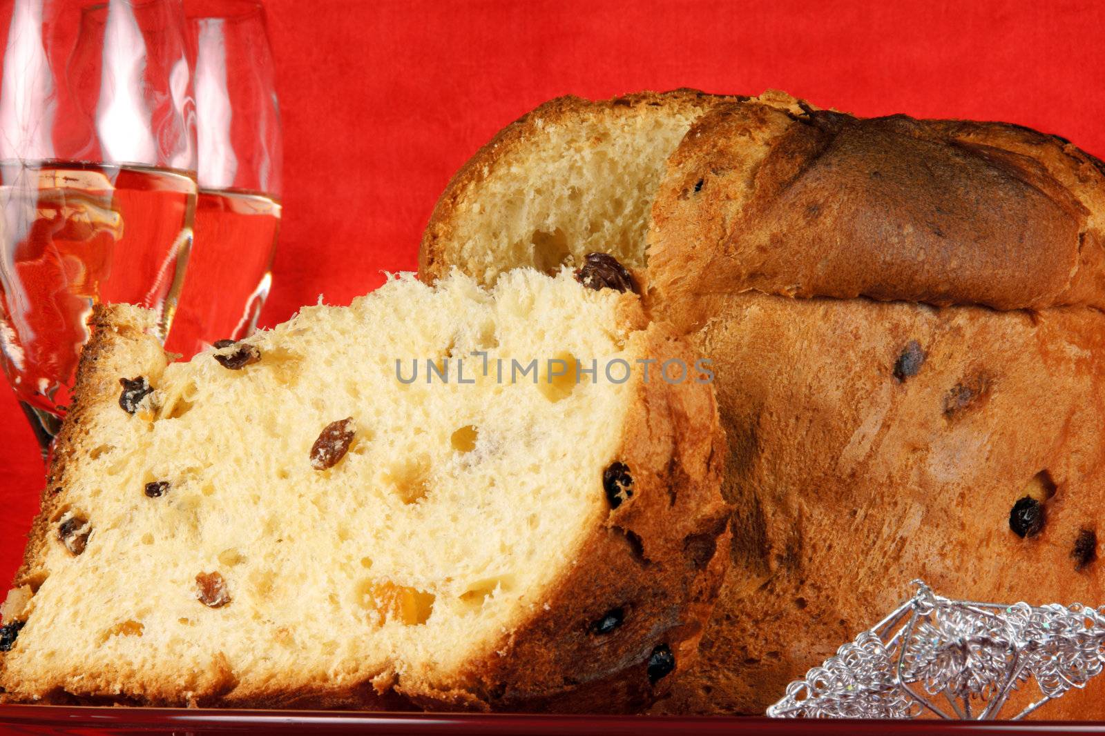 Panettone the italian Christmas fruit cake served on a red glass plate over a red background with silver star decorations and two glasses of champagne. Selective focus.