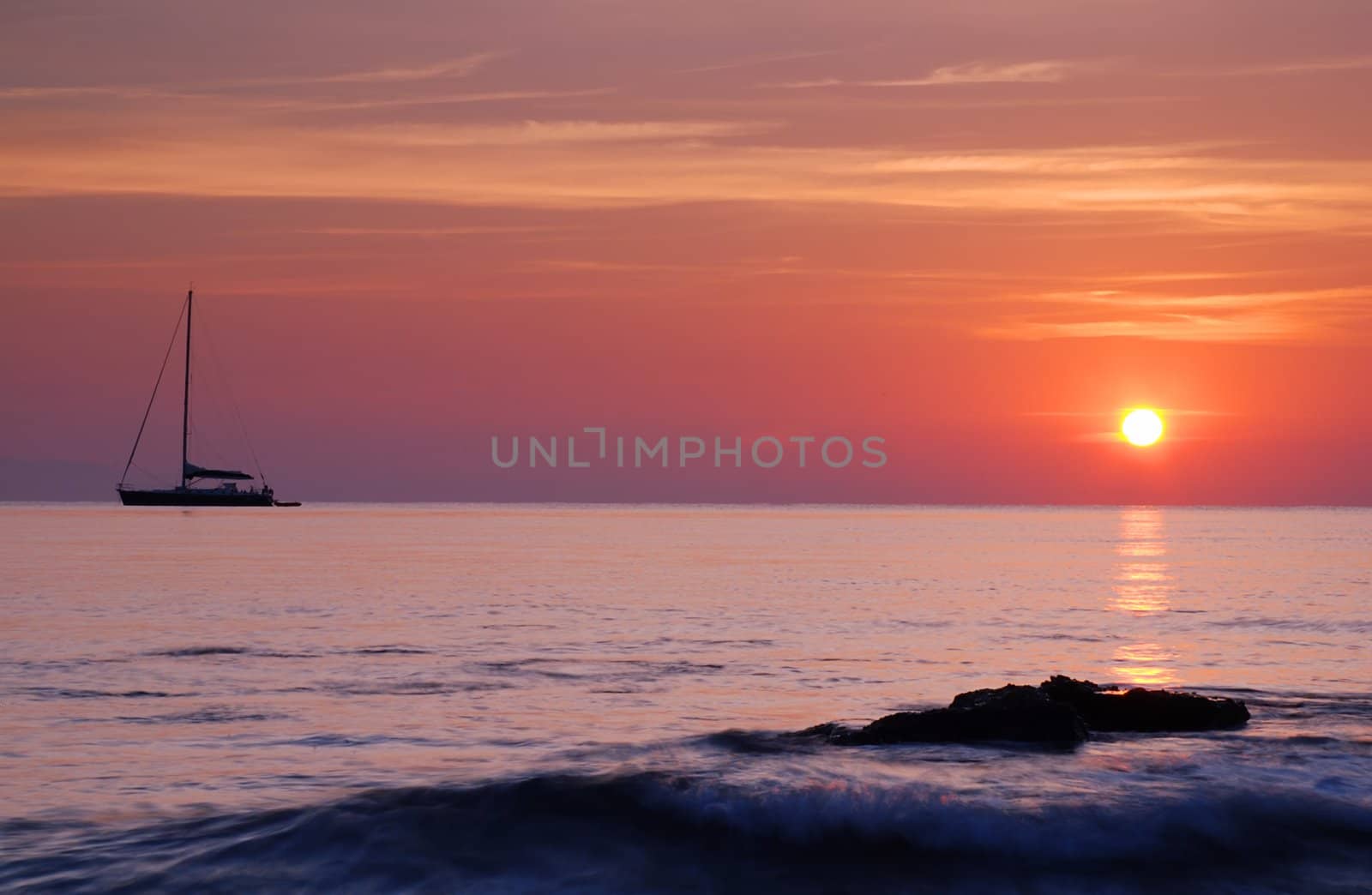 Sailing boat silhouette and rock with surf at sunrise