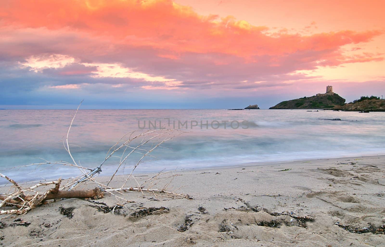 Fairytale sunrise on Sardinia - beach is washed by surf, lighthouse in the back