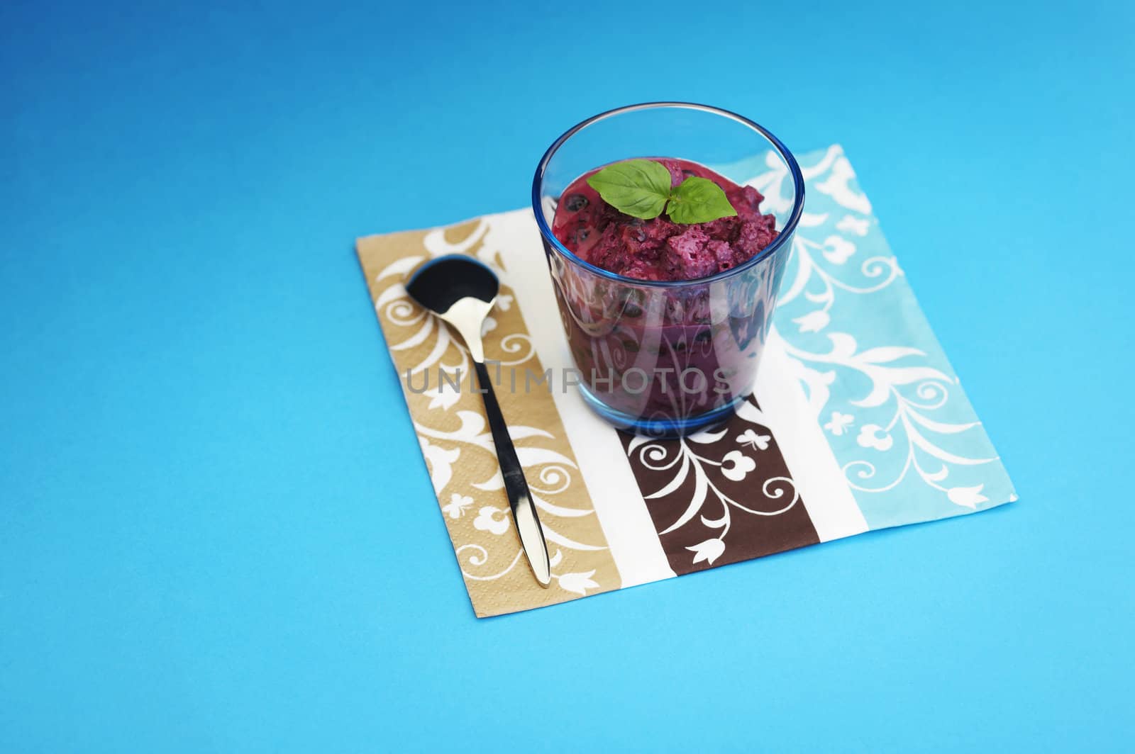 Glass of home made bilberry yogurt with bread crumbs over a blue background