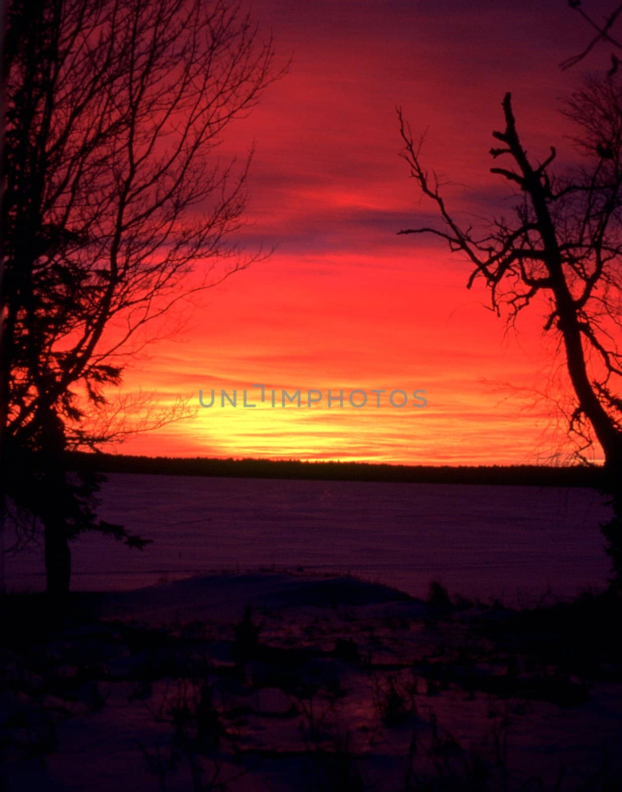 The sunset over a frozen, snowy lake creates vivid shades of red and orange.