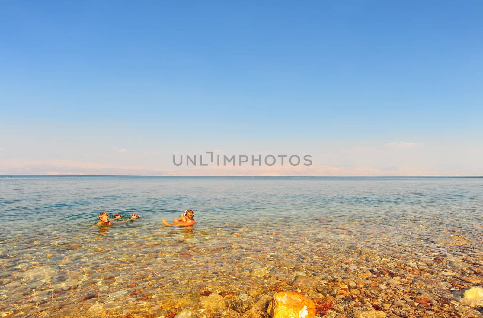 Woman And Boy Relaxing In Dead Sea Laying On Water Surface