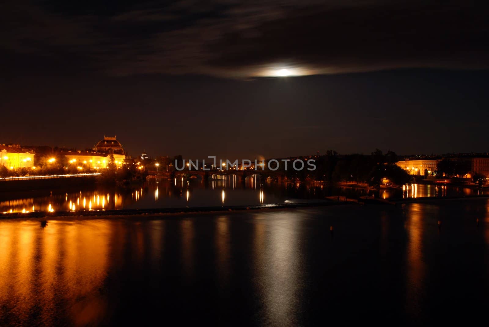 Prague in the night with a full moon mirroring in the river Moldau