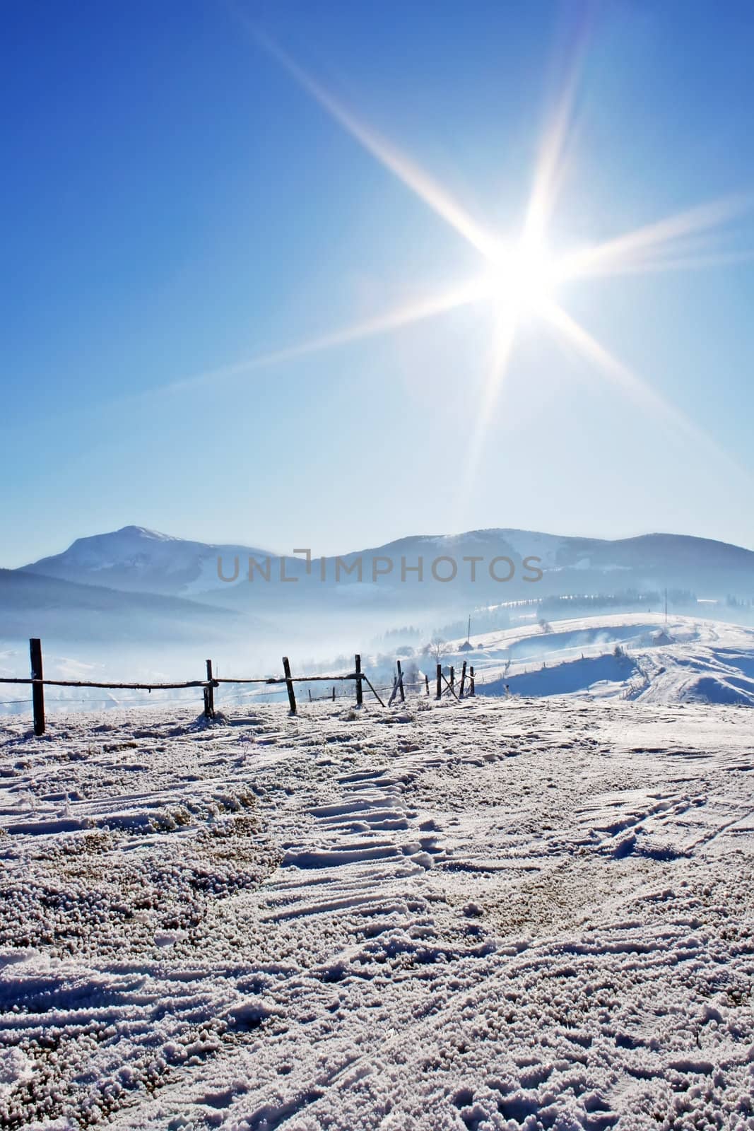 Wooden fence in snow covered mountains under shiny sun