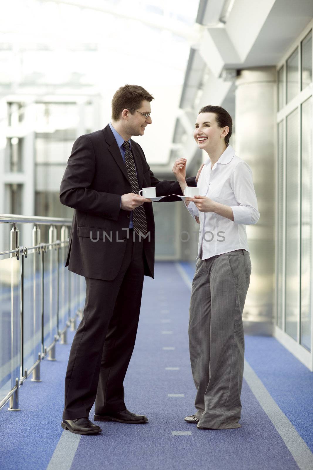 Business couple portrait - young man and woman having coffe on modern office corridor
