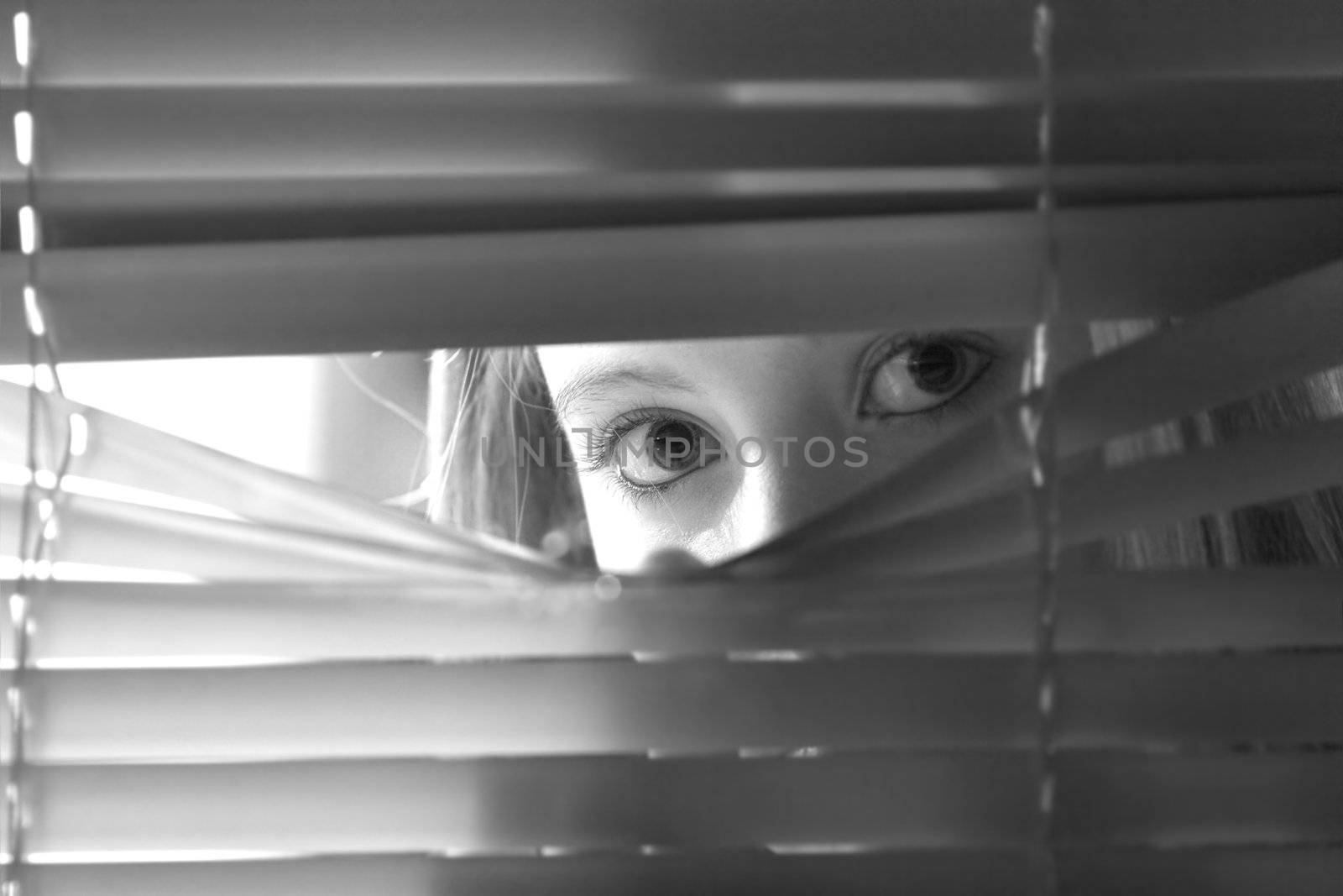 Young female looking through window blinds at night.(shallow depth of field)