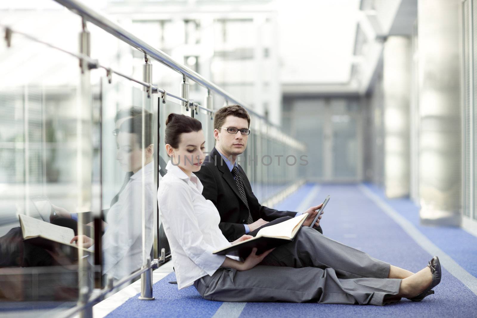 Business couple portrait - young man and woman working together on the floor of modern office corrdor