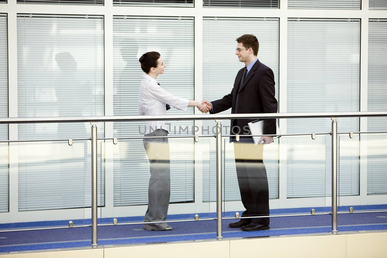 Businessman and businesswoman shaking hands on modern office corridor.