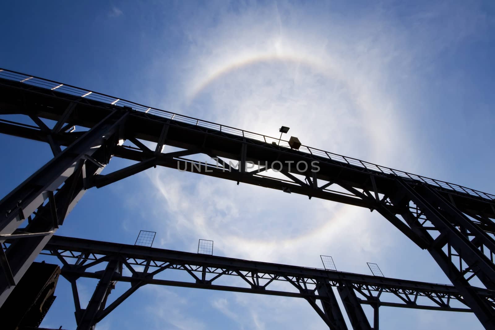 An amazing sun halo in blue cloudy sky above metal bridge