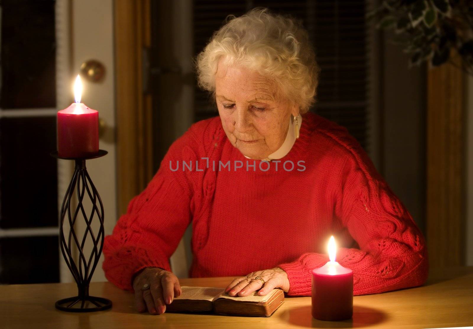 Elderly lady sitting in candlelight reading the bible