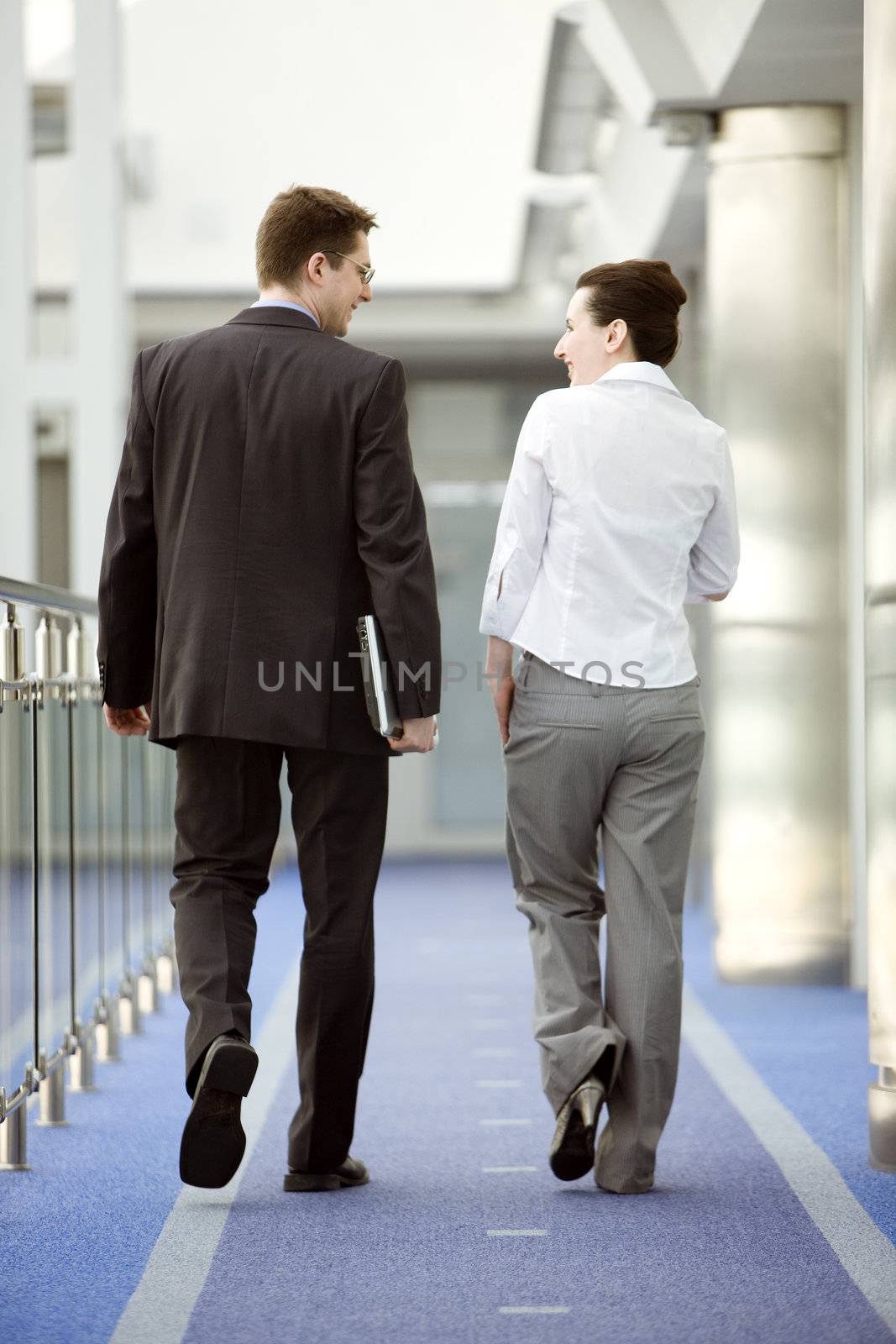 Businessman and businesswoman walking and talking on modern office corridor.