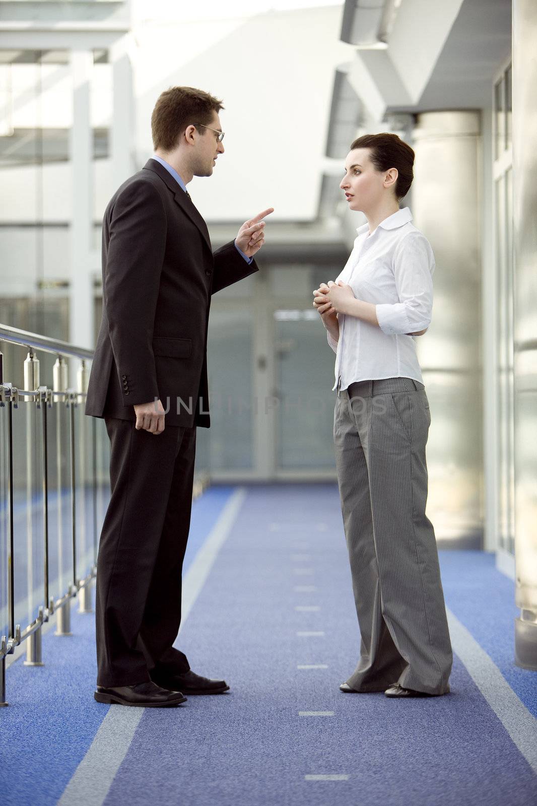 Businessman and businesswoman having argument in modern office building corridor