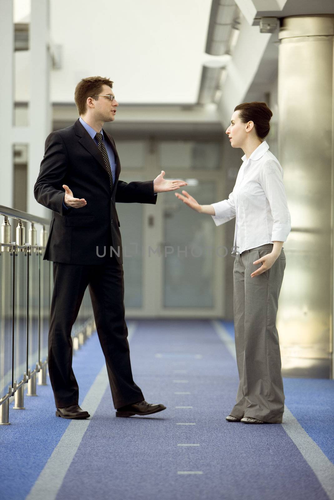 Businessman and businesswoman having argument in modern office corridor