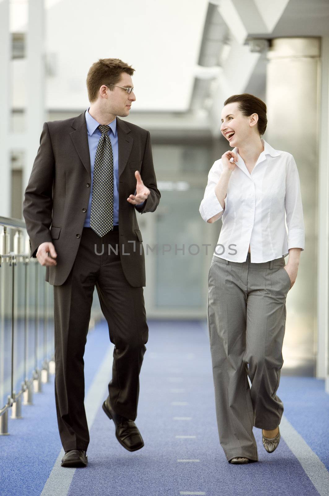 Businessman and businesswoman walking and talking on modern office corridor.