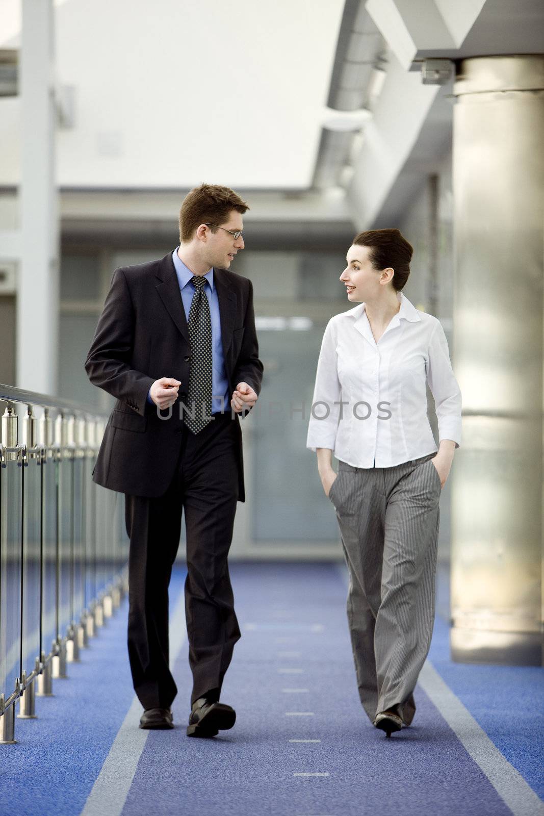 Businessman and businesswoman walking and talking on modern office building corridor.