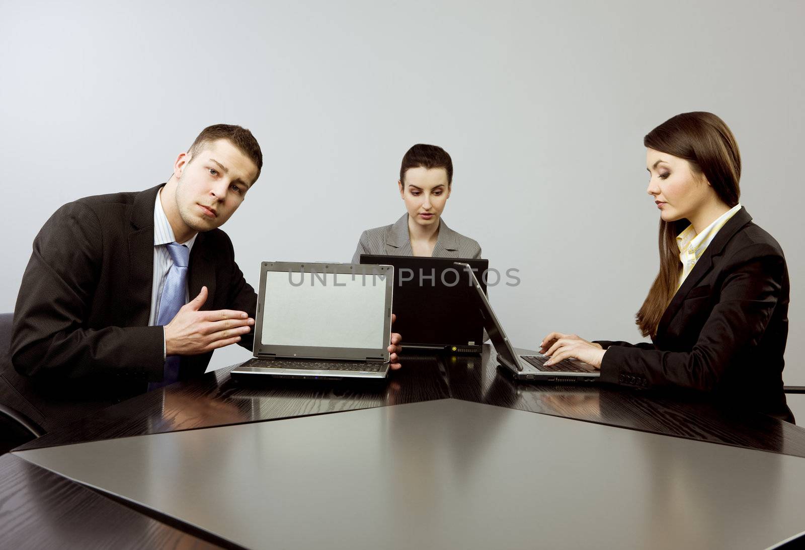 Business group portrait - Young man presenting something on the screen of his computer and two women working on their laptops