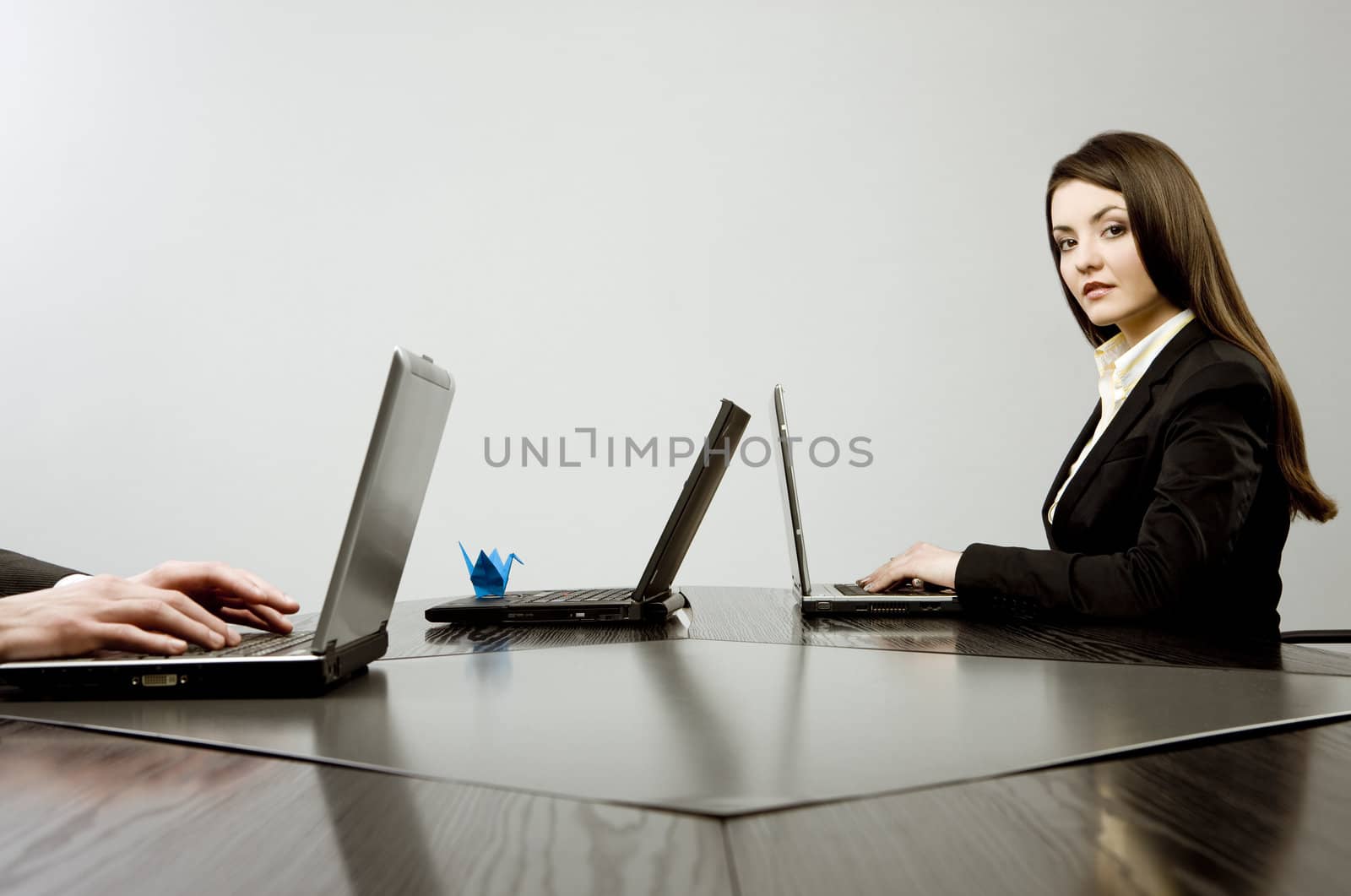Beautiful young businesswoman sitting at a desk with three laptops with blue origami on one of them and human hands on another one