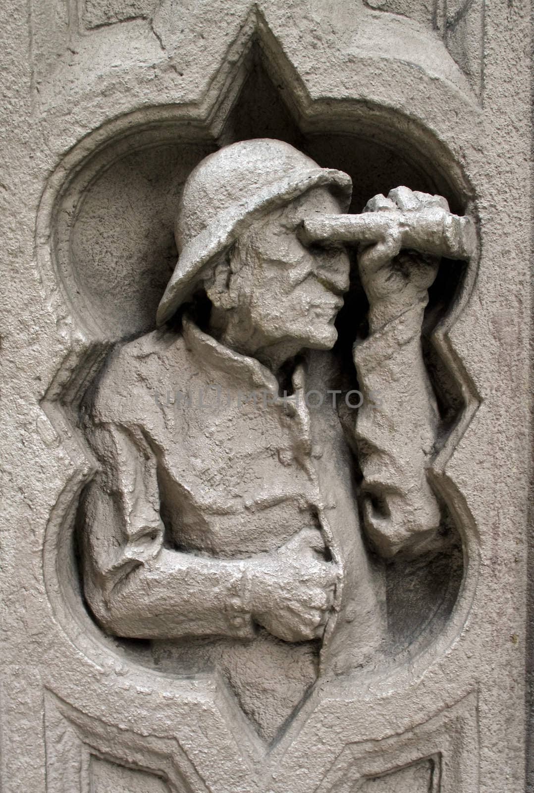 Carving of an old man looking through binoculars on the outside of a building