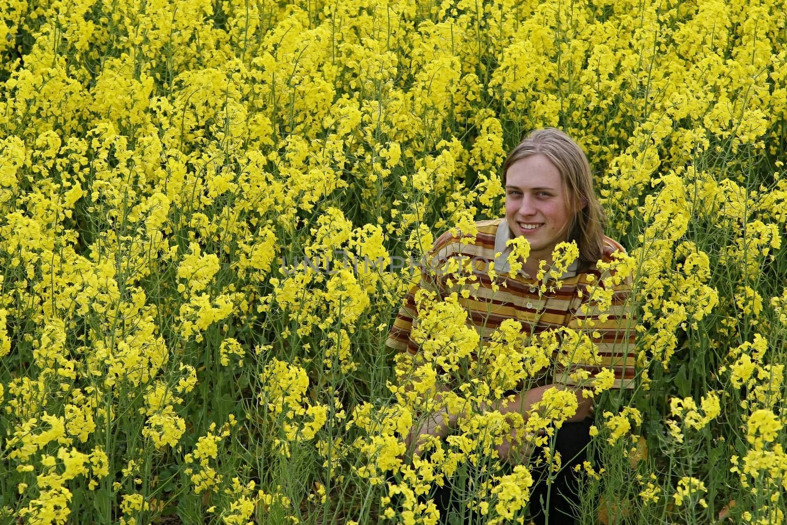 Happy and smiling young man in the yellow flower meadow.
