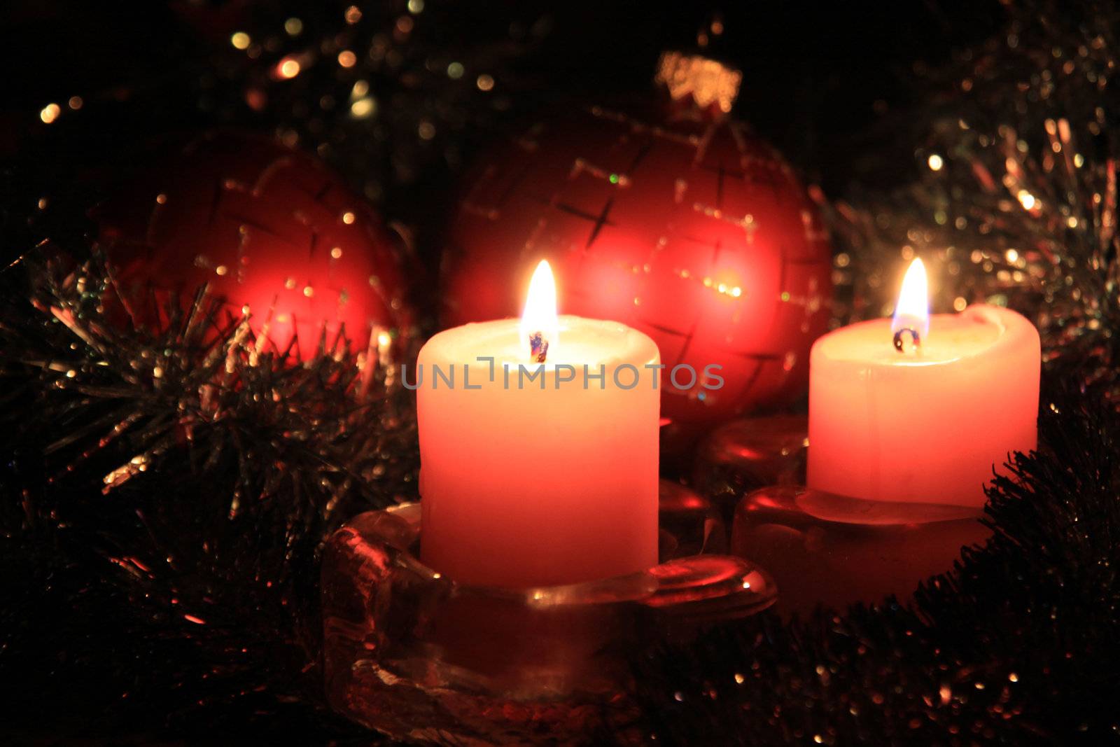 Christmas candles against a tinsel and red spheres

