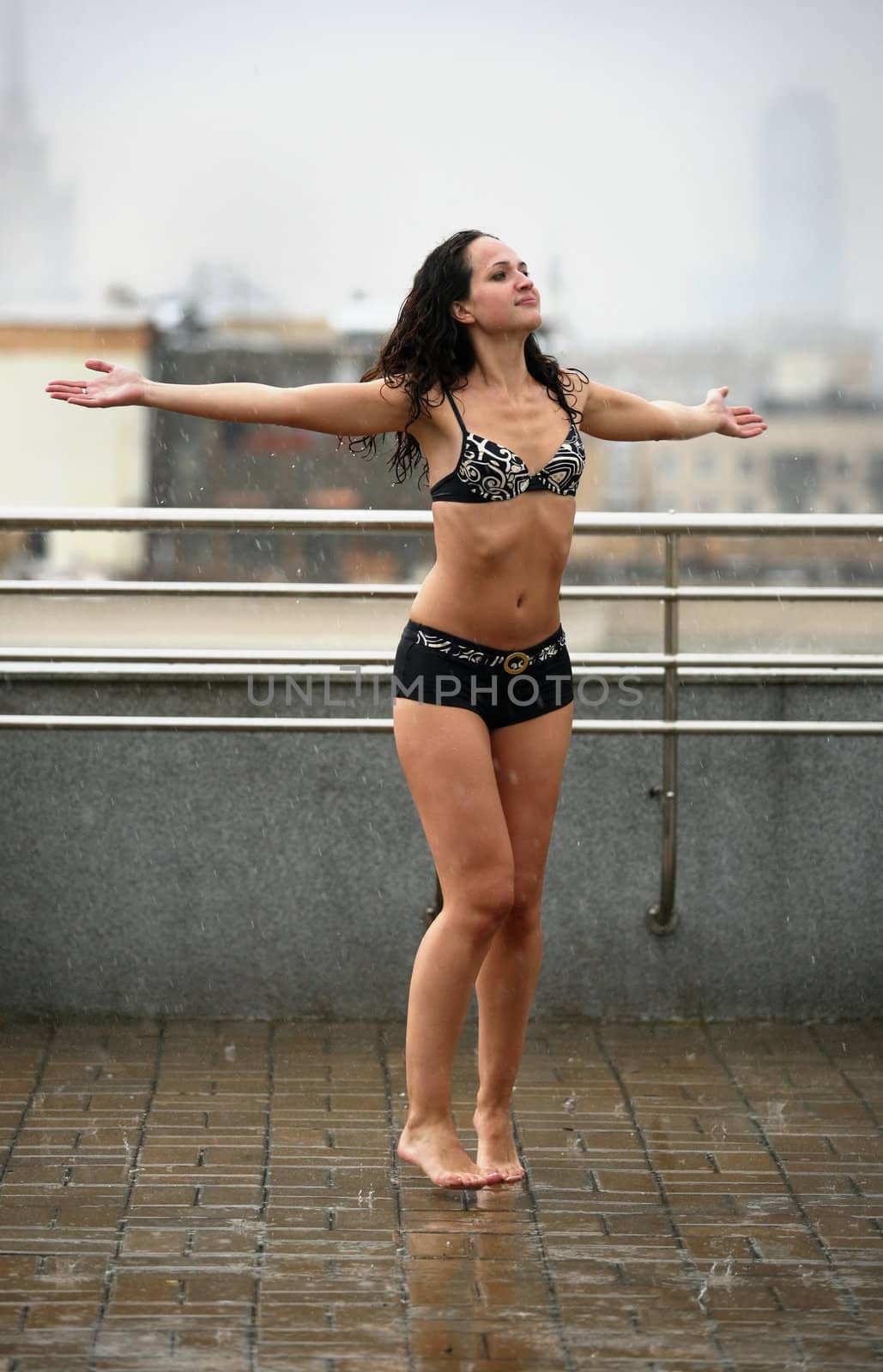 The beautiful woman dances on a roof under a rain
