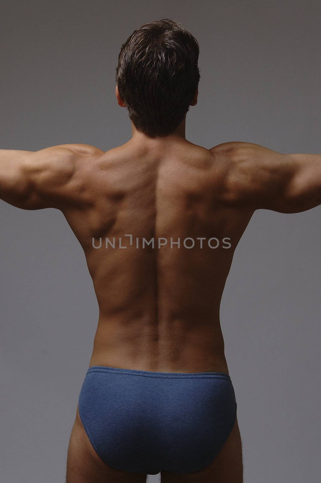 Back of man in underwear with arms extended out to show muscular back definition.