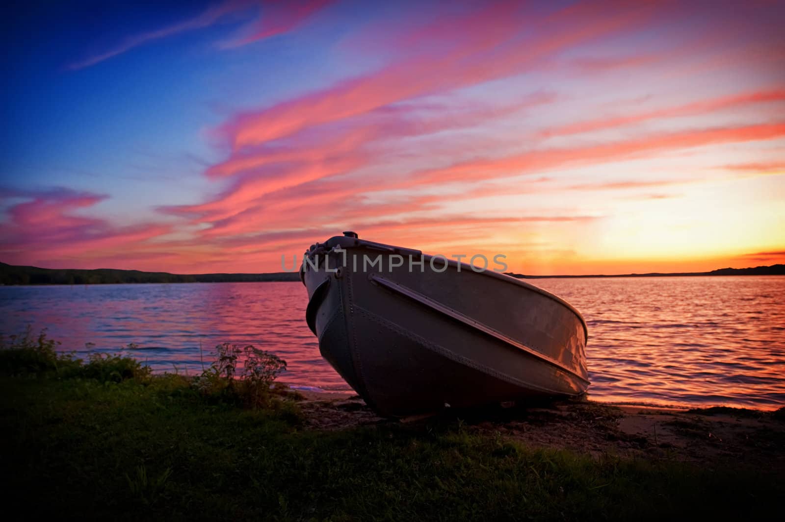 Fishing boat pulled up onto shore of a lake at sunset