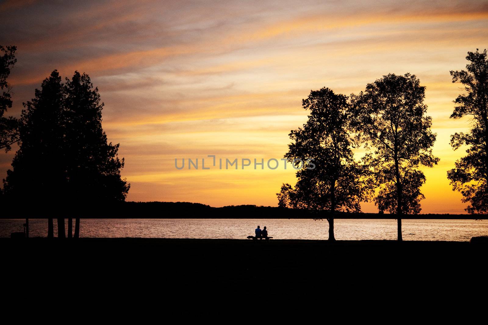 Elderly couple, silhouetted,  sitting on a bench by lake at sunset