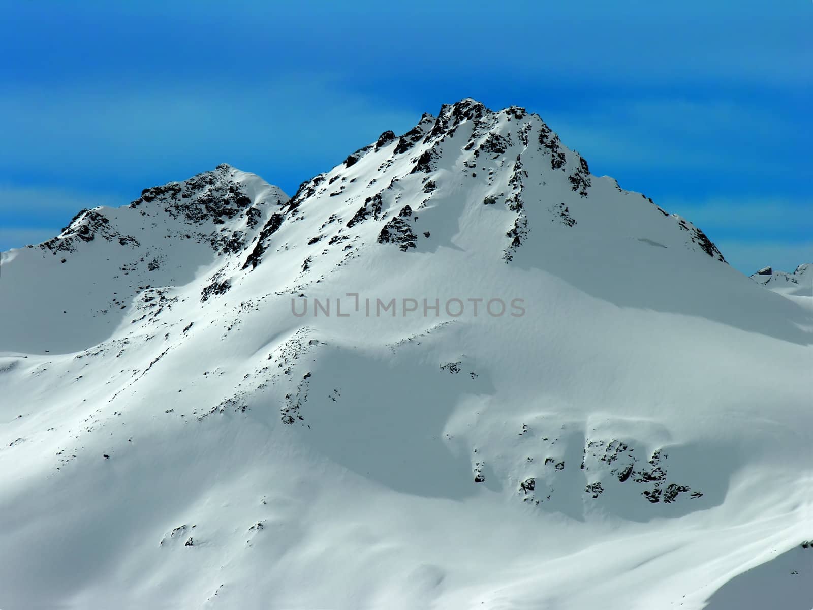 Snow-covered mountain tops on a background of the blue sky.
          