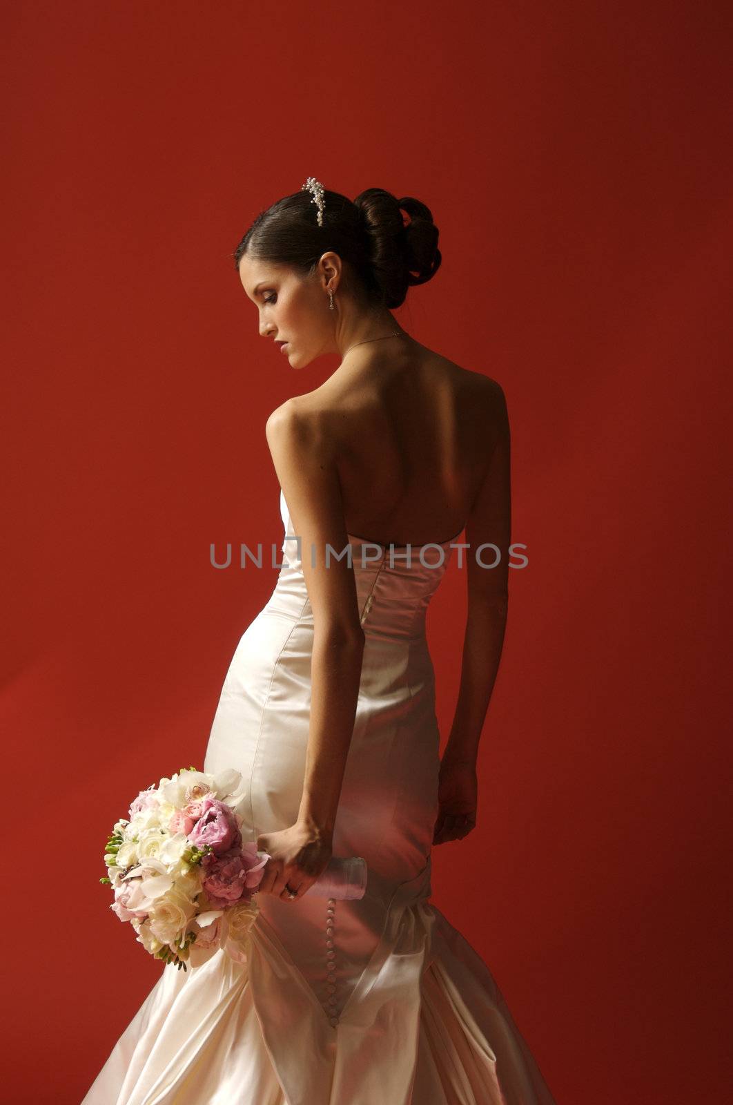 Image of a bride with body turned toward red wall looking down and to the side at bouquet