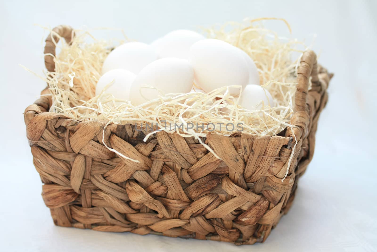 Wicker basket with hay and white eggs